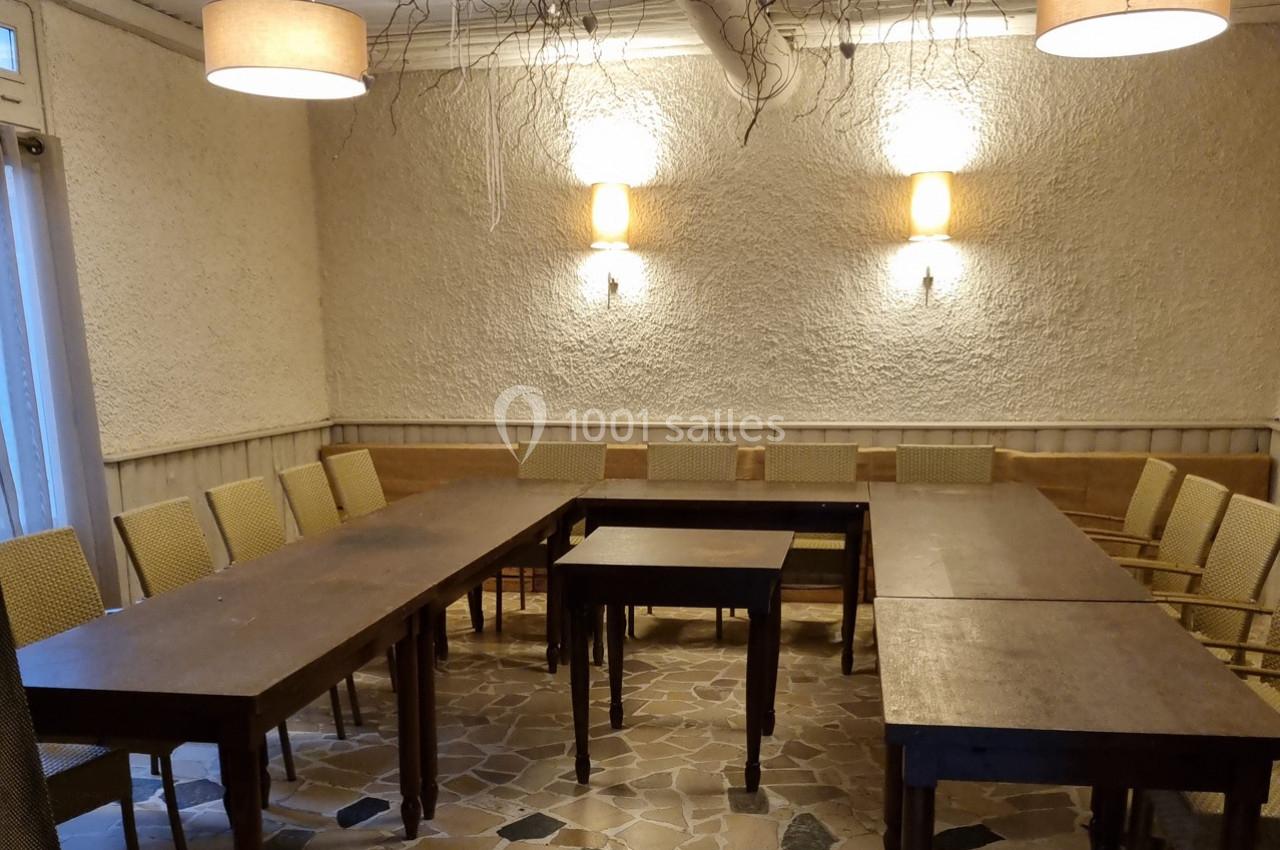 Salle de réunion avec tables en bois disposées en U, chaises en osier et éclairage mural chaleureux.