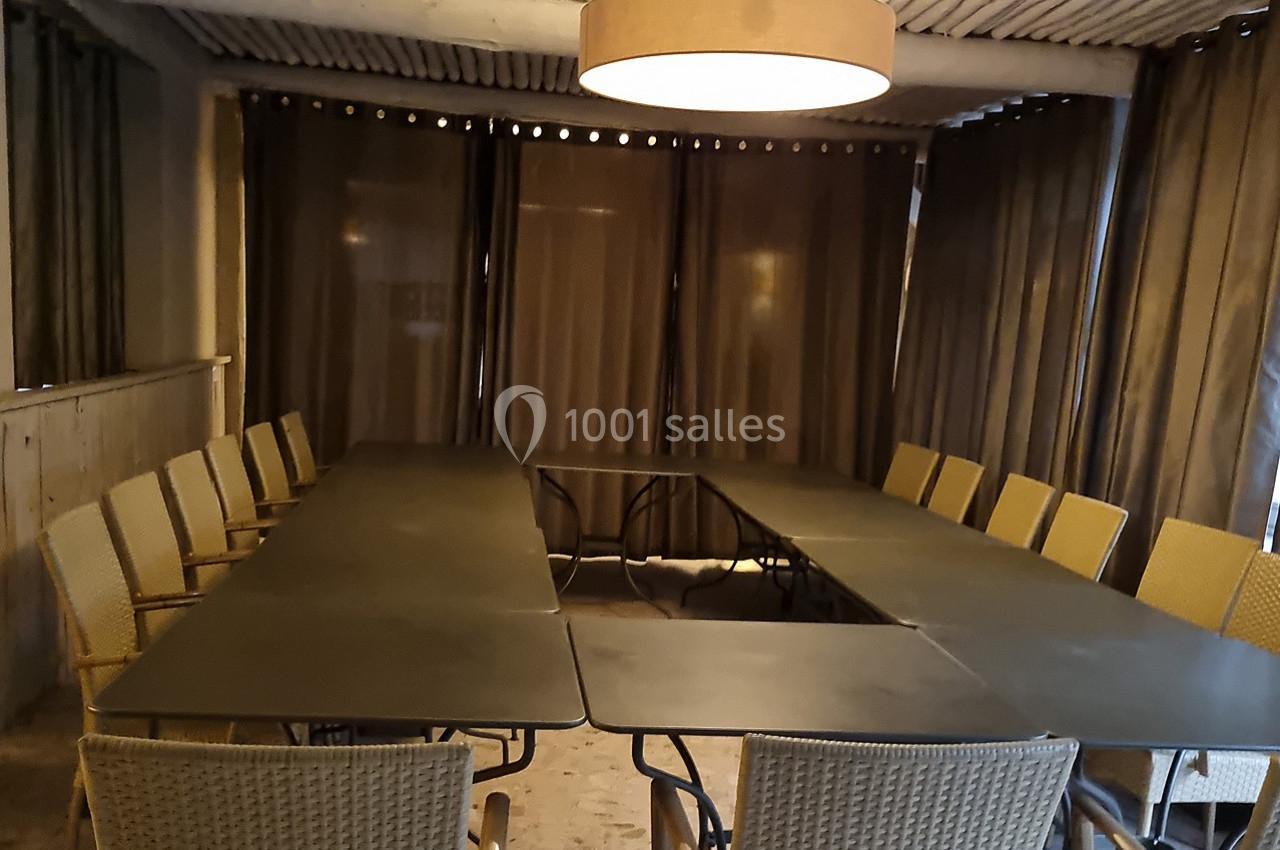 Salle de réunion avec une grande table en U entourée de chaises en osier et éclairée par une suspension centrale.