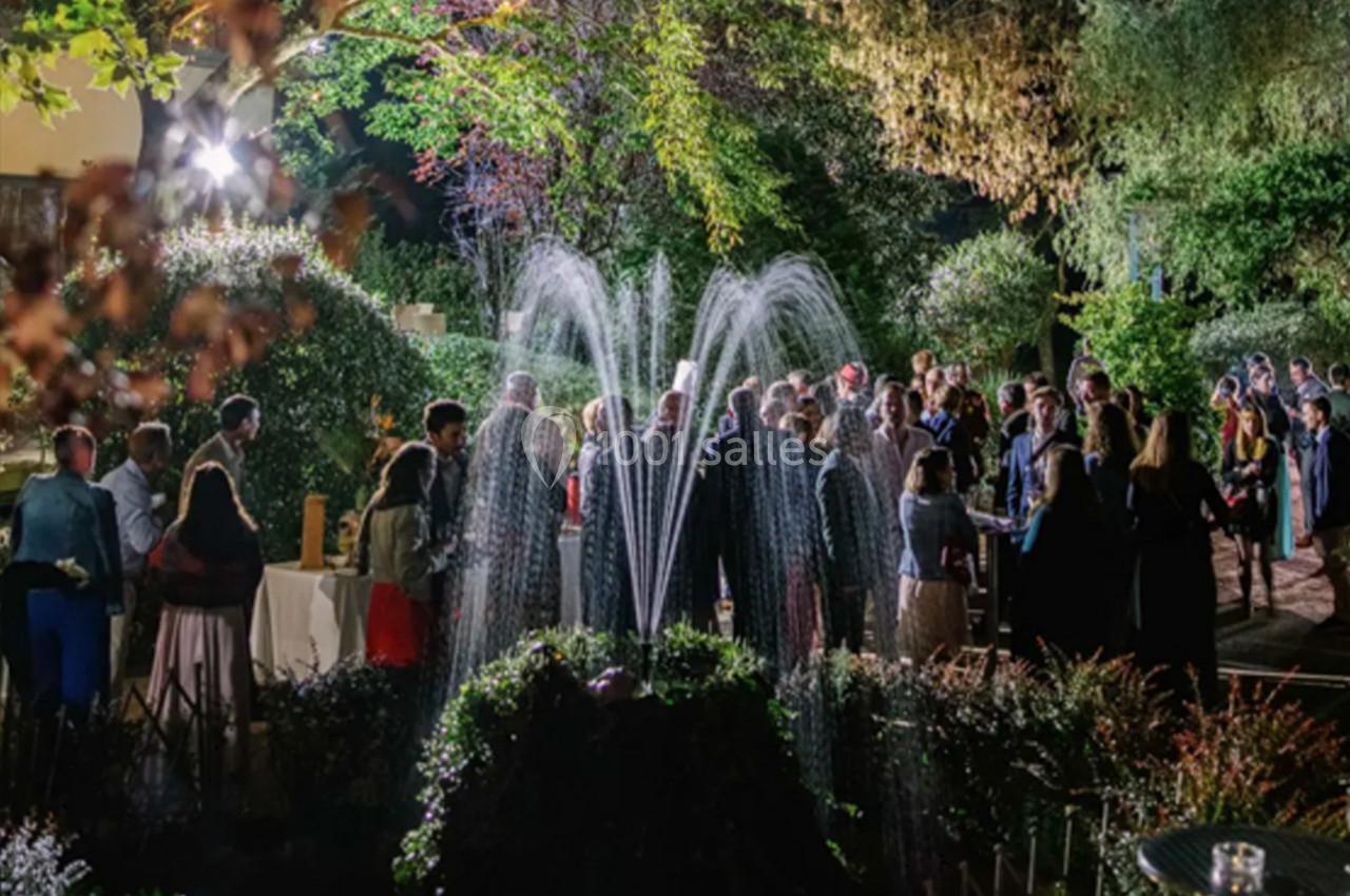 Groupe de personnes rassemblées en soirée dans un jardin éclairé, avec une fontaine illuminée au premier plan.