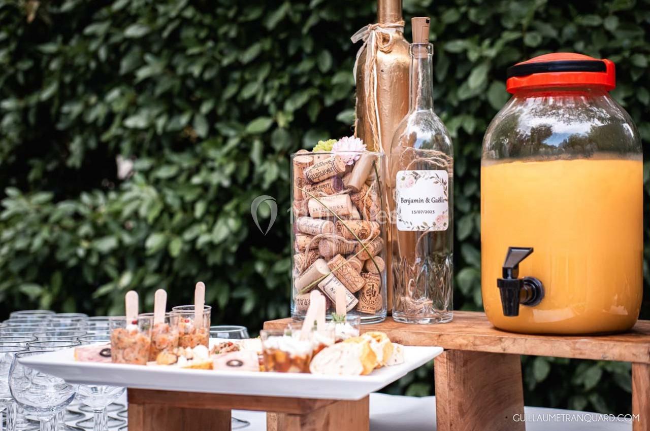 Buffet extérieur avec boissons, verrines, bouteille de vin, carafe de jus et décorations en bouchons de liège.