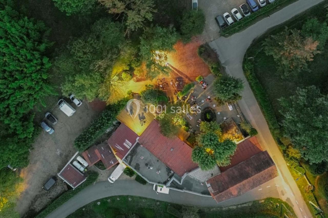 Vue aérienne d'un bâtiment entouré d'arbres, avec une terrasse éclairée et des voitures stationnées à proximité.