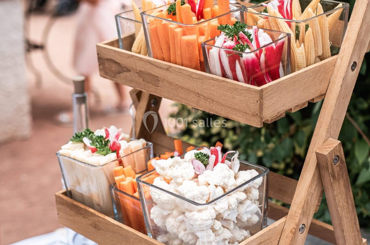 Plateau en bois avec des verrines contenant des légumes frais coupés, comme carottes, radis, chou-fleur et mini-épis de maïs.