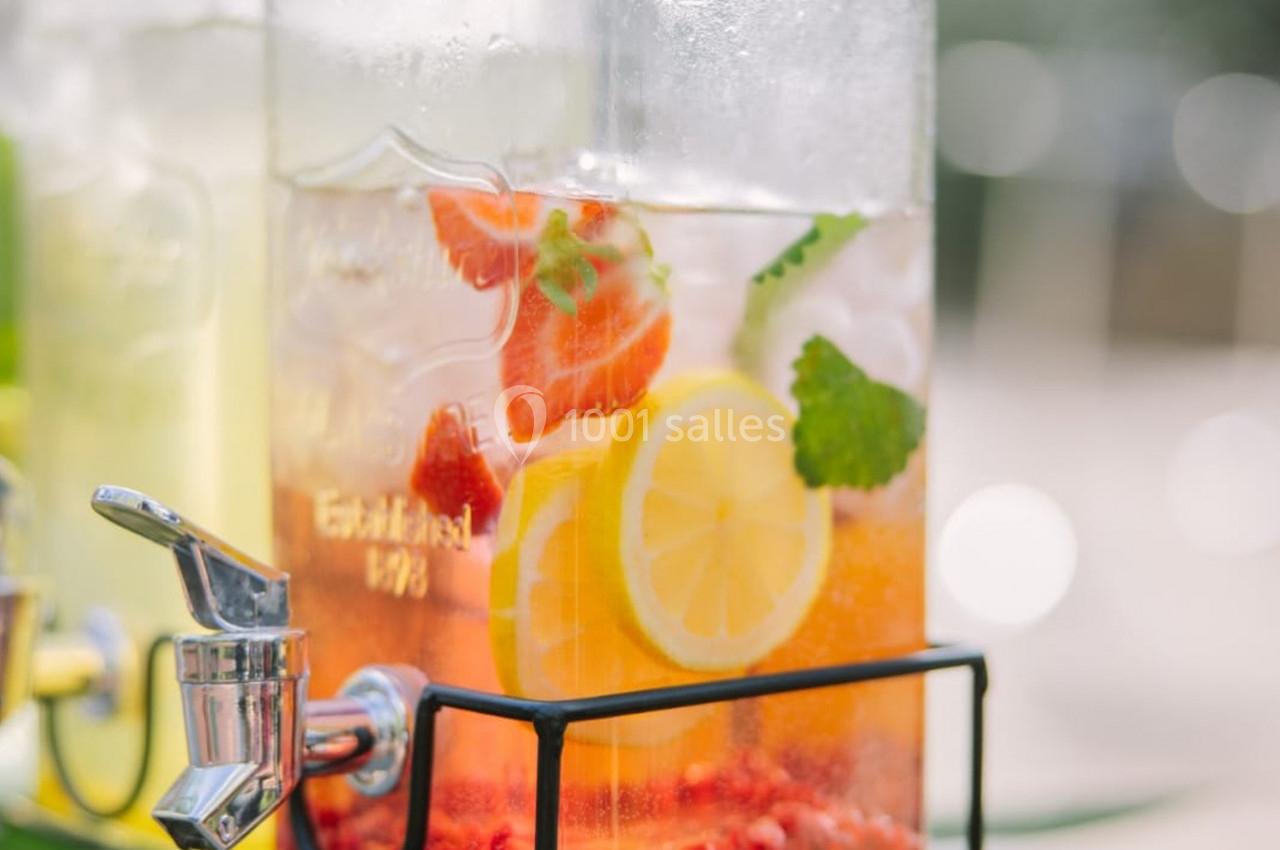 Distributeur de boisson contenant une infusion d'eau avec des tranches de citron, fraises et feuilles de menthe.