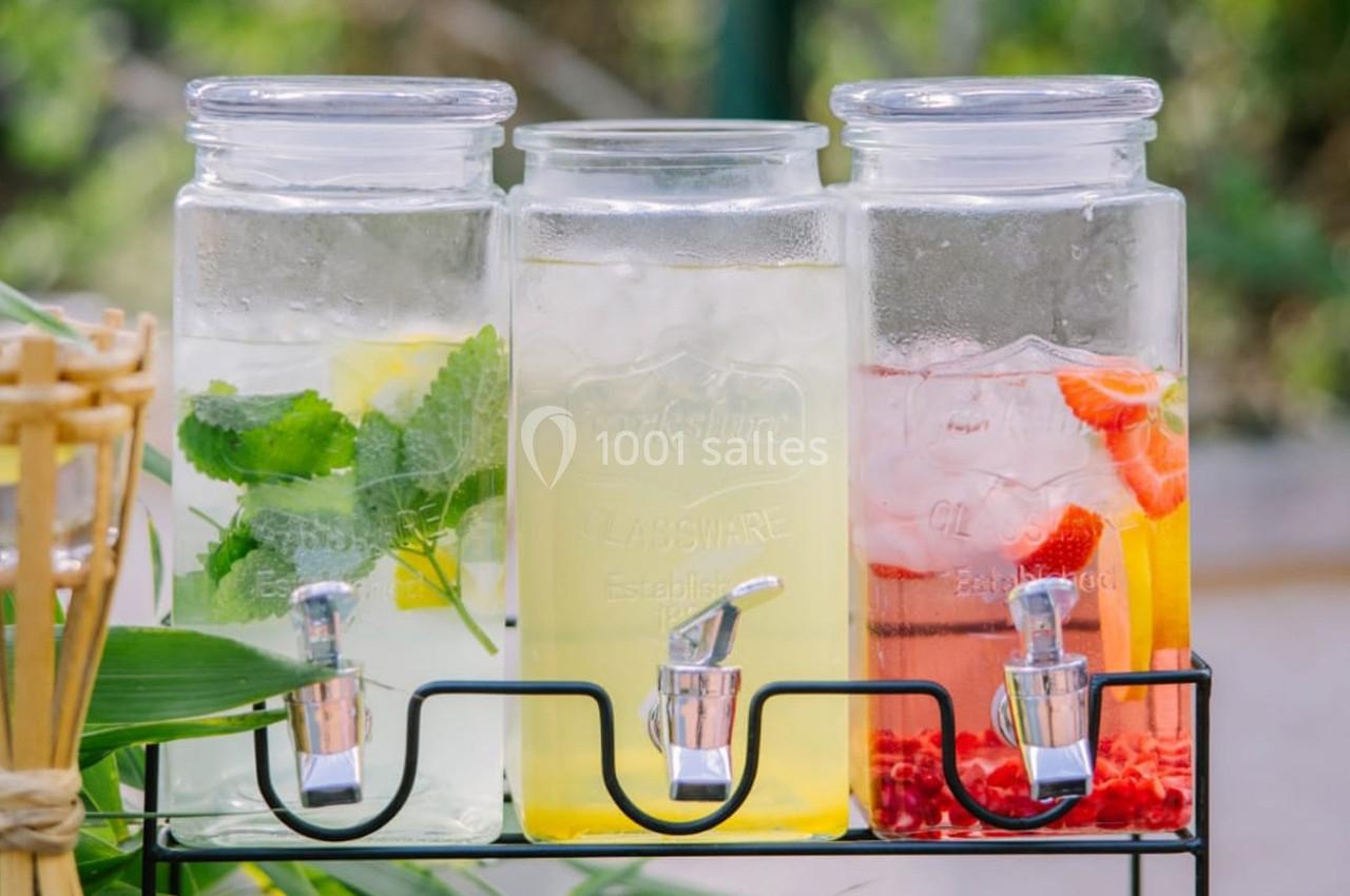 Trois distributeurs en verre contenant des boissons infusées aux fruits et herbes, posés sur un support métallique.