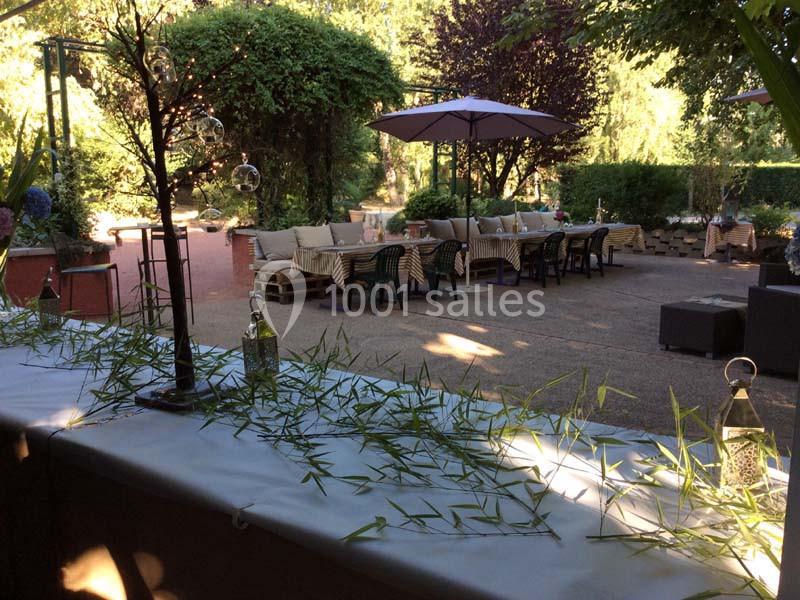 Terrasse aménagée avec tables, chaises et parasols, entourée de végétation et éclairée par la lumière naturelle.