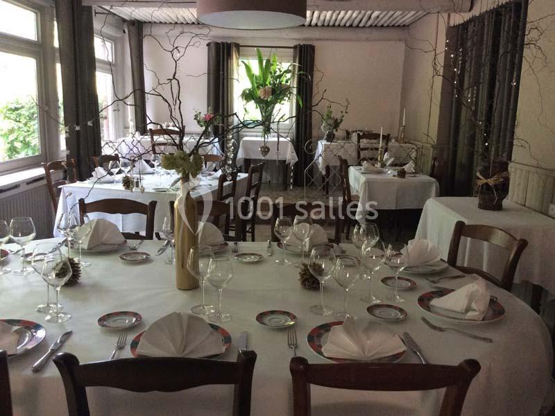 Salle de restaurant décorée avec des tables dressées, nappes blanches, vaisselle élégante et arrangements floraux.