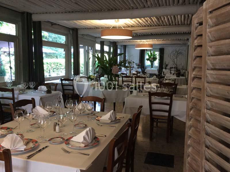 Salle de restaurant lumineuse avec tables dressées, nappes blanches, chaises en bois et décoration végétale.