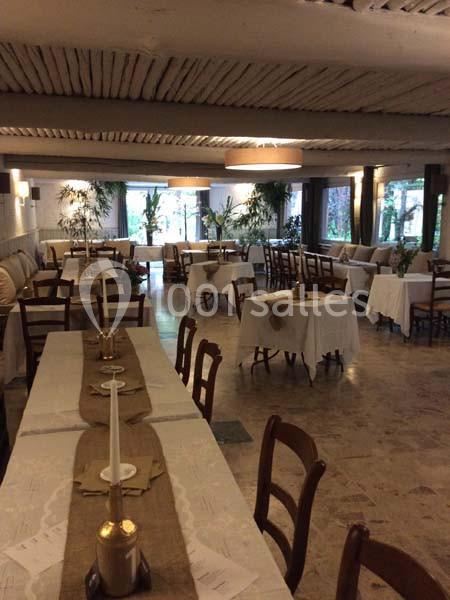 Salle de restaurant décorée avec des tables dressées, nappes blanches et bougies, éclairée par des fenêtres donnant sur un…