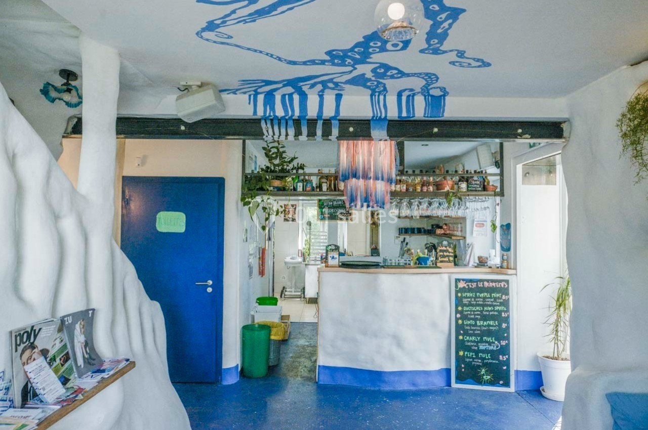 Intérieur d'un café avec un comptoir, des étagères de bouteilles, des murs blancs sculptés et une décoration bleue au…