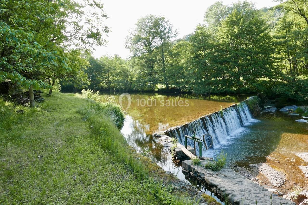 Petite cascade sur une rivière entourée de verdure, avec un chemin herbeux sur la gauche.