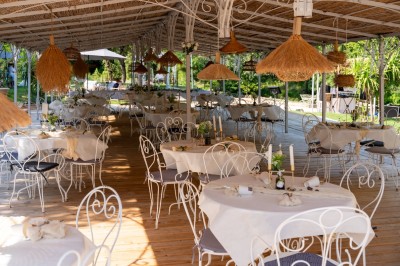 Table décorée pour un événement, avec nappes blanches, fleurs, bougies et couverts dorés dans un cadre extérieur.