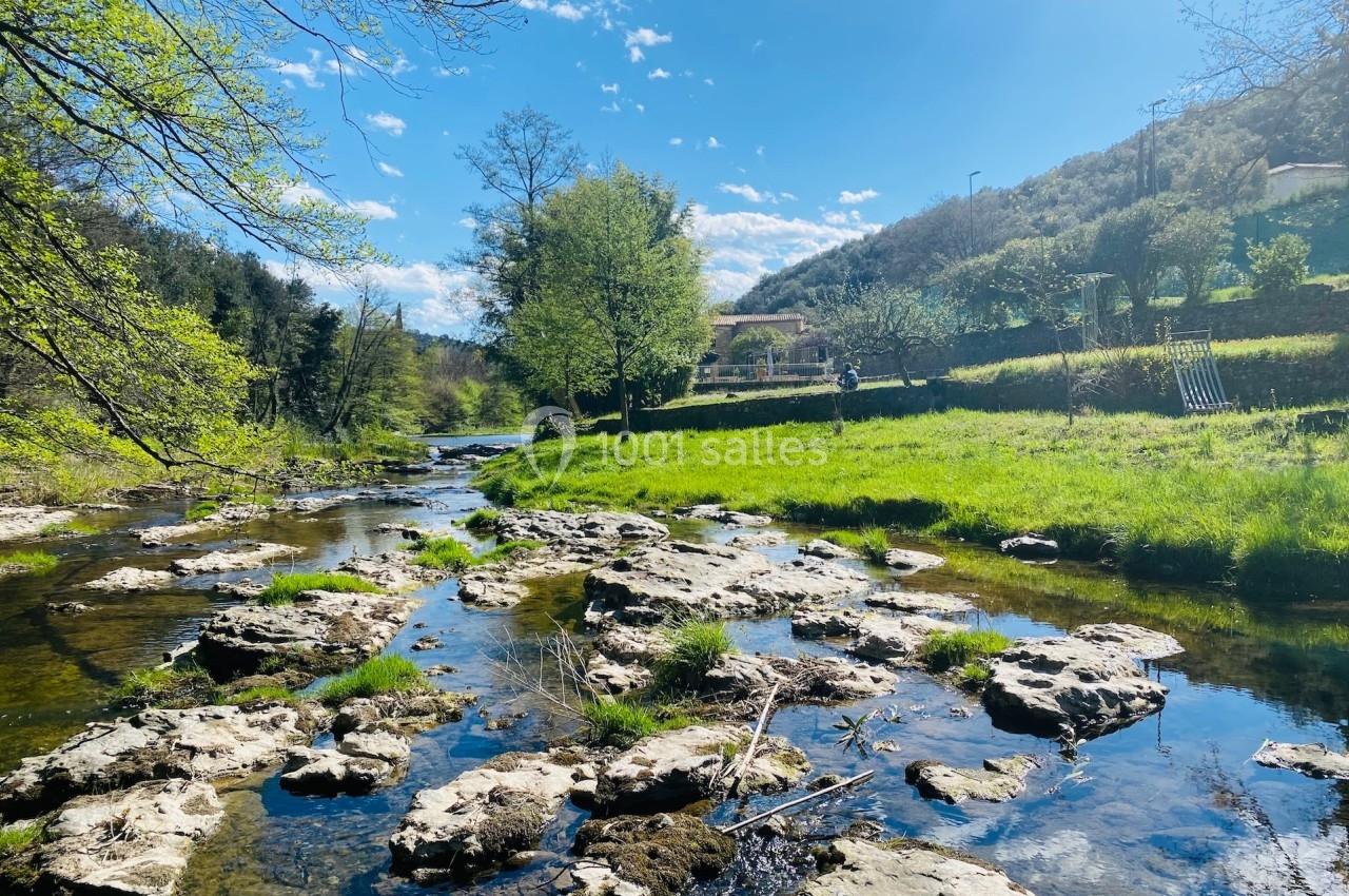 Rivière peu profonde bordée de verdure et de rochers sous un ciel bleu parsemé de nuages.