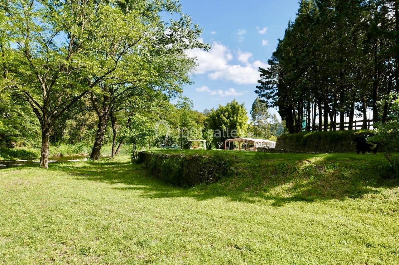 Pelouse verdoyante bordée d'arbres, avec des structures légères en arrière-plan sous un ciel partiellement nuageux.