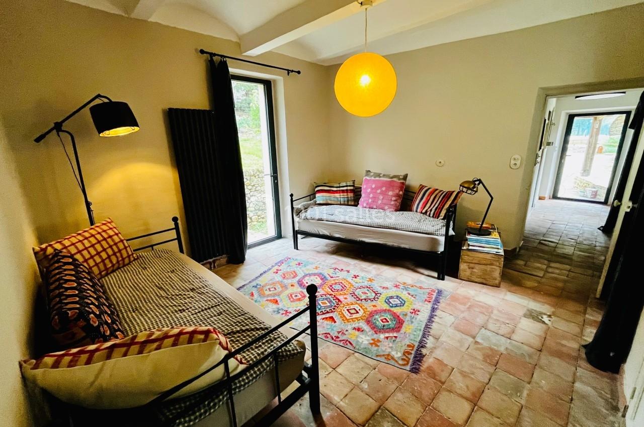 Deux canapés-lits avec coussins colorés dans une pièce lumineuse au sol en terre cuite, éclairée par une suspension jaune.