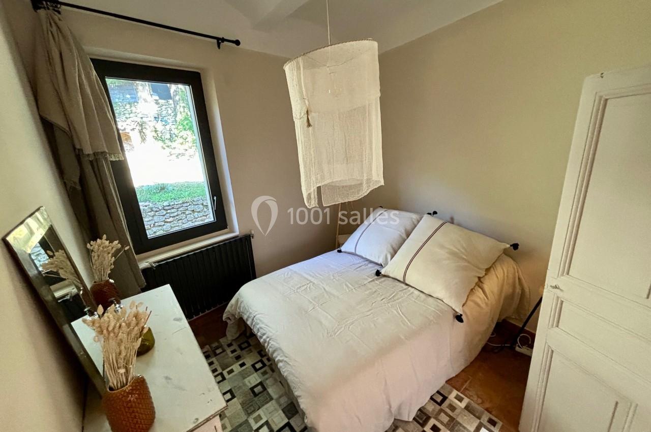 Chambre lumineuse avec lit double, linge blanc, armoire, commode et fenêtre donnant sur un jardin.