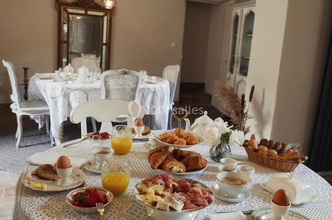Table dressée pour un petit-déjeuner avec viennoiseries, fruits, œufs, jus d'orange et café dans une salle élégante.