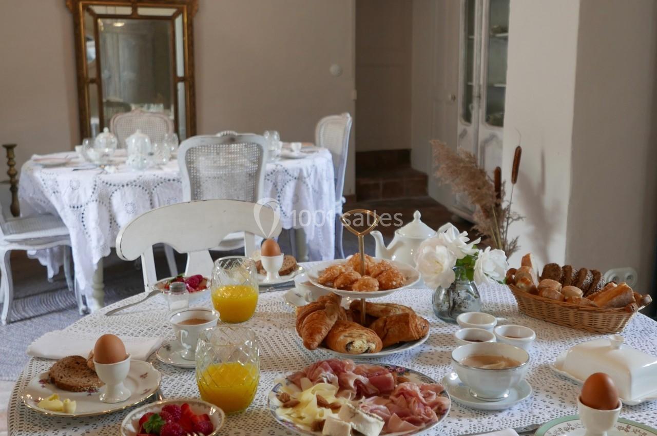 Table dressée pour un petit-déjeuner avec viennoiseries, fruits, œufs, jus d'orange et vaisselle élégante dans une salle…