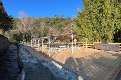 Table décorée pour un événement, avec nappes blanches, fleurs, bougies et couverts dorés dans un cadre extérieur.