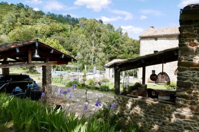 Rivière bordée de rochers et de végétation sous un ciel bleu, avec une maison partiellement visible en arrière-plan.