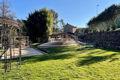 Rivière bordée de rochers et de végétation sous un ciel bleu, avec une maison partiellement visible en arrière-plan.