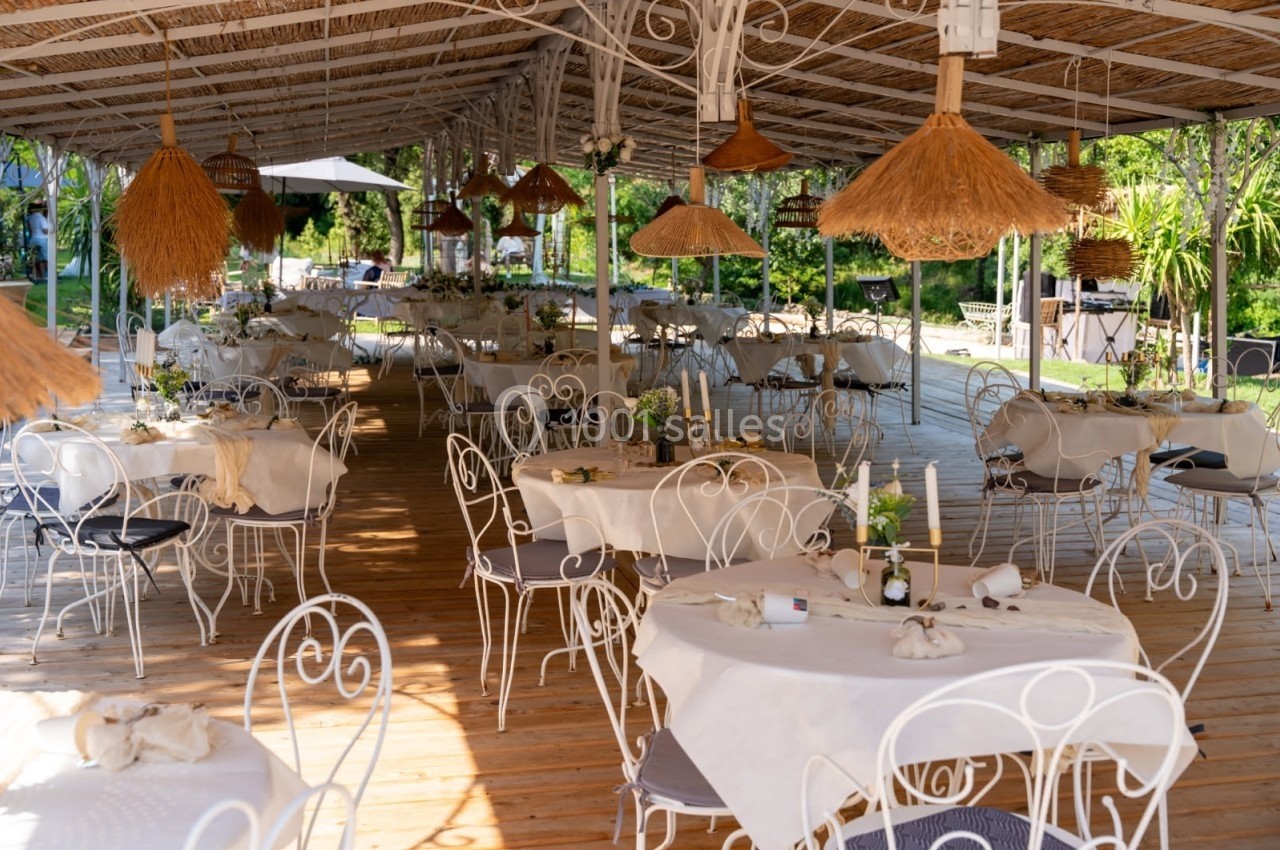 Terrasse couverte d'un restaurant avec des tables dressées, chaises en fer forgé et décorations en matériaux naturels.