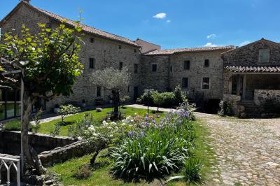 Rivière bordée de rochers et de végétation sous un ciel bleu, avec une maison partiellement visible en arrière-plan.