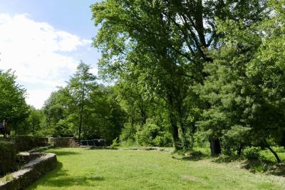Rivière bordée de rochers et de végétation sous un ciel bleu, avec une maison partiellement visible en arrière-plan.