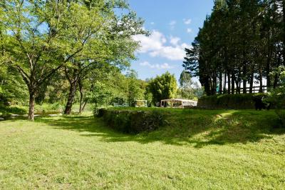 Rivière bordée de rochers et de végétation sous un ciel bleu, avec une maison partiellement visible en arrière-plan.
