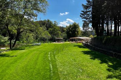 Rivière bordée de rochers et de végétation sous un ciel bleu, avec une maison partiellement visible en arrière-plan.