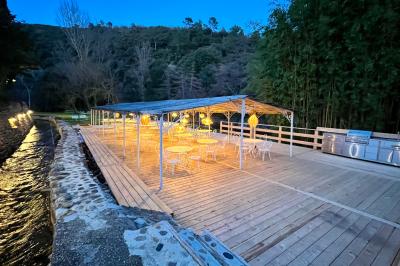 Rivière bordée de rochers et de végétation sous un ciel bleu, avec une maison partiellement visible en arrière-plan.