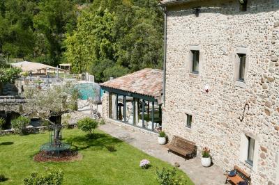 Rivière bordée de rochers et de végétation sous un ciel bleu, avec une maison partiellement visible en arrière-plan.