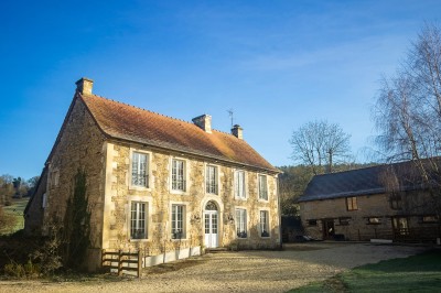 Chambre chaleureuse avec lits, canapé, fauteuils en osier, table basse et éclairage tamisé, décor rustique.