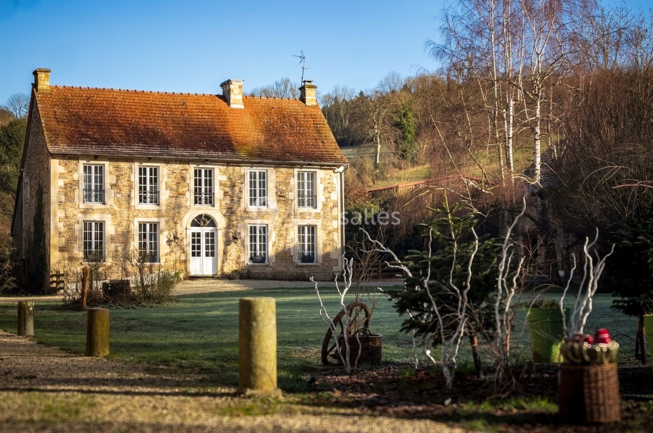 Maison en pierre avec toit en tuiles, entourée de végétation et située dans un paysage rural ensoleillé.