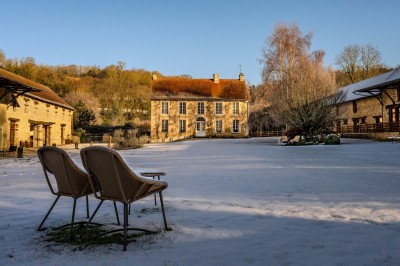 Chambre chaleureuse avec lits, canapé, fauteuils en osier, table basse et éclairage tamisé, décor rustique.