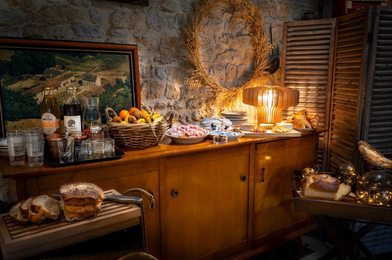 Buffet rustique avec fruits, pain, charcuterie, boissons et décorations chaleureuses sur un meuble en bois.