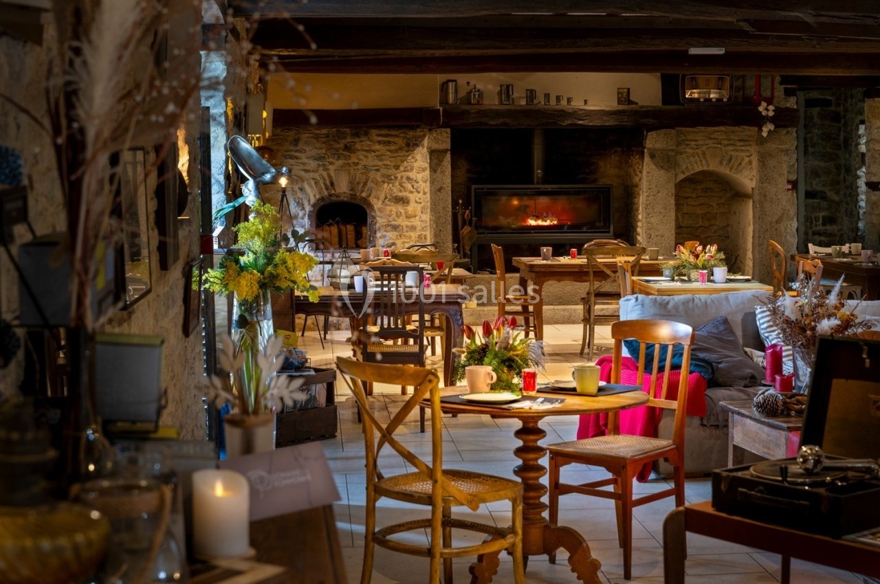 Salle chaleureuse avec cheminée allumée, tables en bois décorées de fleurs et ambiance rustique.
