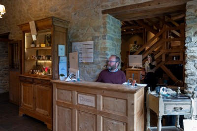 Chambre chaleureuse avec lits, canapé, fauteuils en osier, table basse et éclairage tamisé, décor rustique.