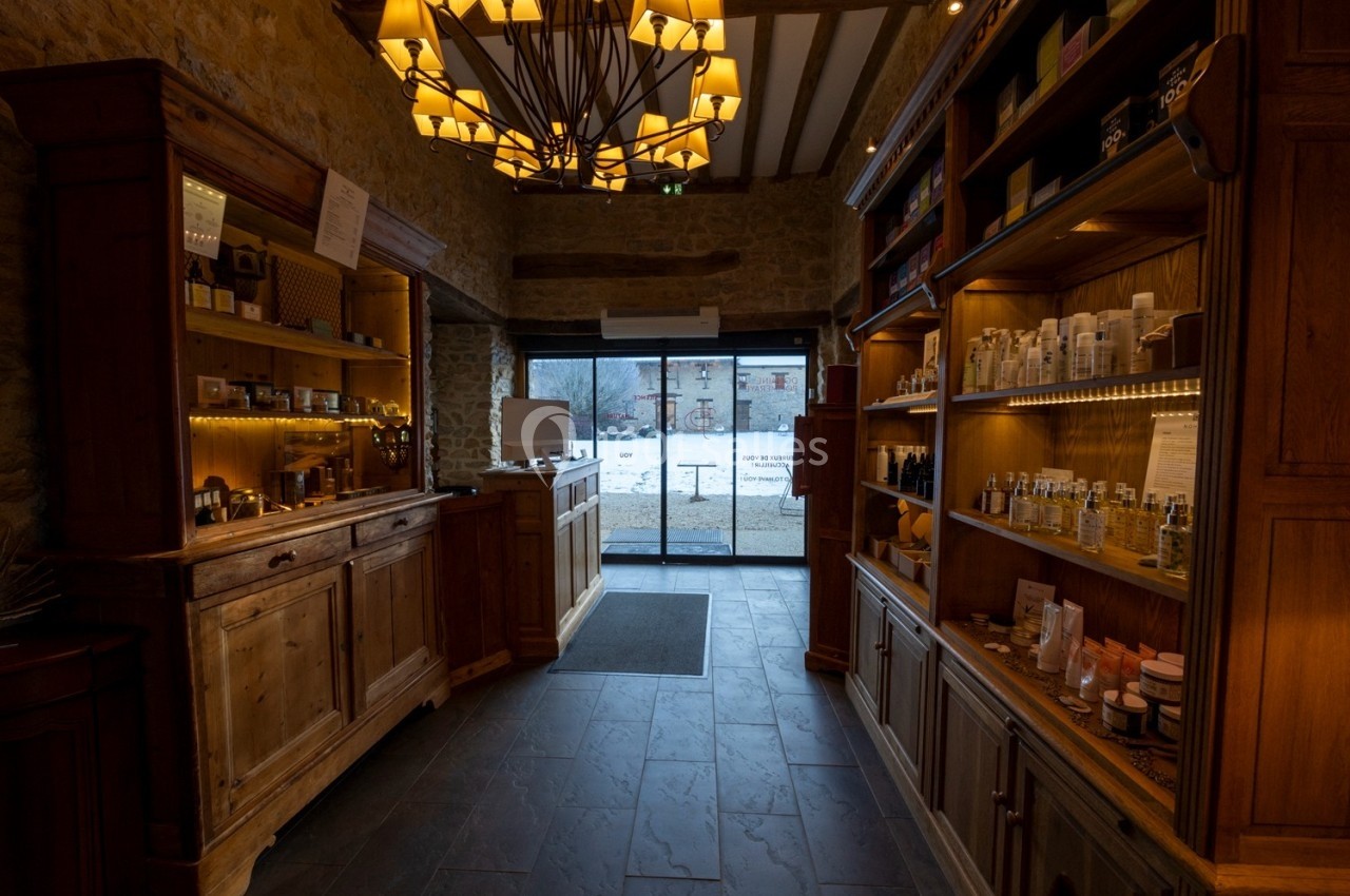 Intérieur d'une boutique avec des étagères en bois remplies de produits, éclairée par un lustre, vue sur l'extérieur enneigé.