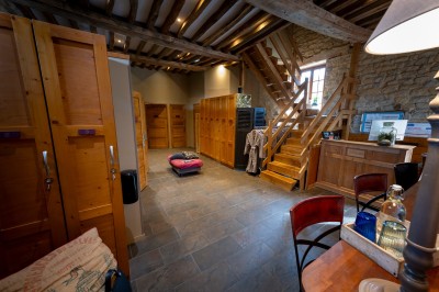 Chambre chaleureuse avec lits, canapé, fauteuils en osier, table basse et éclairage tamisé, décor rustique.