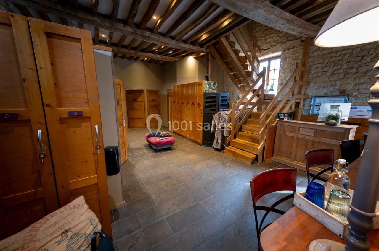 Vestiaire en bois avec casiers, banc central, escalier en bois et murs en pierre dans un espace chaleureux.