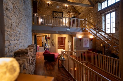 Chambre chaleureuse avec lits, canapé, fauteuils en osier, table basse et éclairage tamisé, décor rustique.