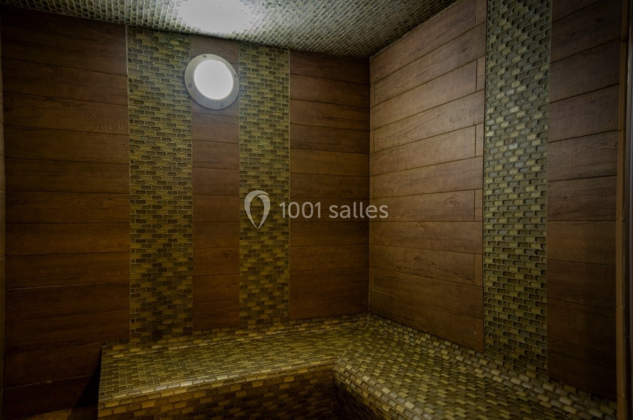 Cabine de sauna avec murs en bois et mosaïque, éclairée par une petite lampe ronde au plafond.