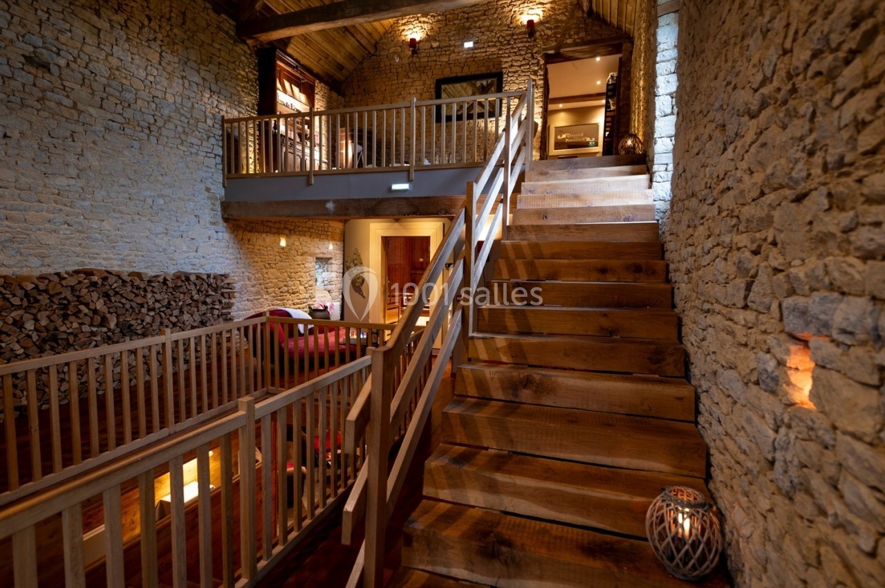 Escalier en bois massif dans une maison en pierre avec mezzanine, éclairage chaleureux et décoration rustique.