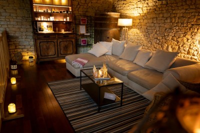 Chambre chaleureuse avec lits, canapé, fauteuils en osier, table basse et éclairage tamisé, décor rustique.