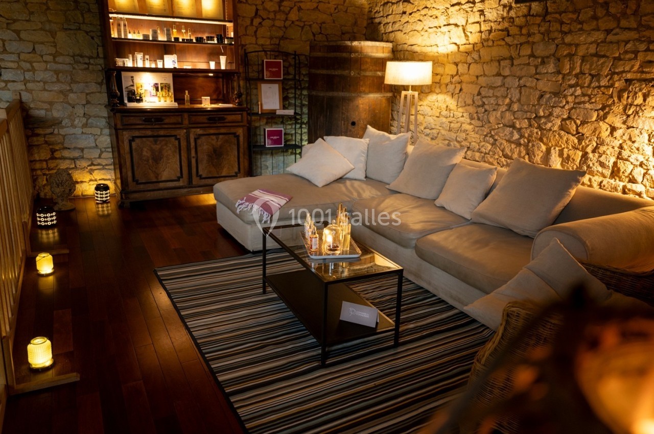 Salon chaleureux avec canapé beige, table basse décorée, éclairage tamisé et murs en pierre apparente.