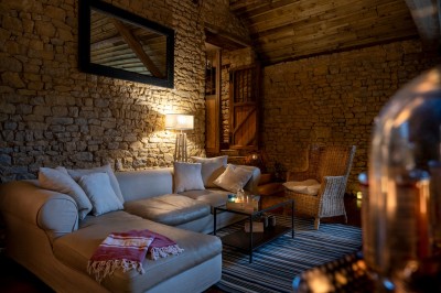 Chambre chaleureuse avec lits, canapé, fauteuils en osier, table basse et éclairage tamisé, décor rustique.