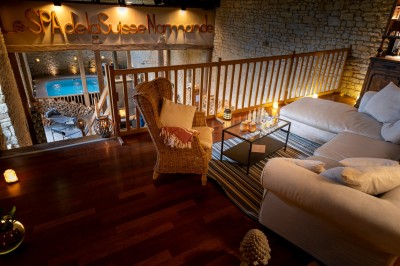 Chambre chaleureuse avec lits, canapé, fauteuils en osier, table basse et éclairage tamisé, décor rustique.