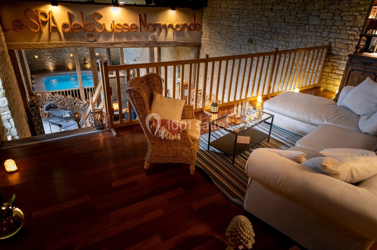 Espace détente chaleureux avec fauteuil en osier, canapé, bougies et vue sur une piscine intérieure éclairée.