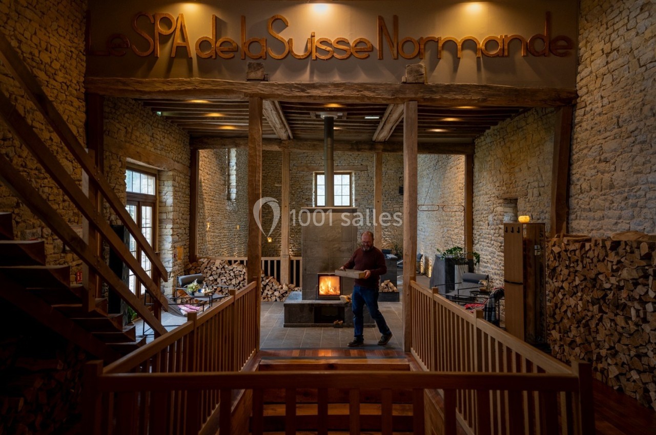 Intérieur d'un spa avec murs en pierre, cheminée centrale allumée et un homme marchant dans un espace chaleureux.