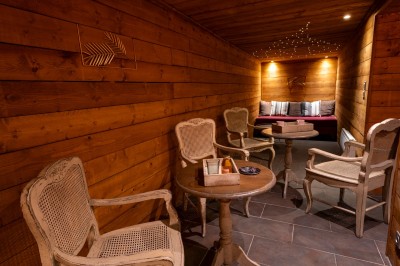 Chambre chaleureuse avec lits, canapé, fauteuils en osier, table basse et éclairage tamisé, décor rustique.